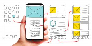 UI development. Adult male hand holding smartphone with wireframed user interface screen prototypes of a mobile application on white background.